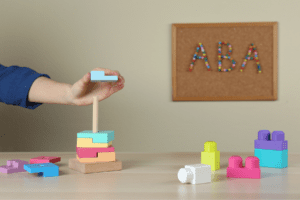 A child's hand engaging in structured play activity with colourful blocks in an ABA therapy session promotes learning.