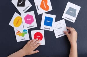 Cards with figures and English words lie on a black background. Children's hands are holding a card. Learning English concept